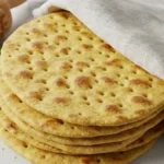 Pain polaire maison cuit, empilé sur une table, avec une serviette par-dessus et un rouleau à piquants en bois posé à côté.
