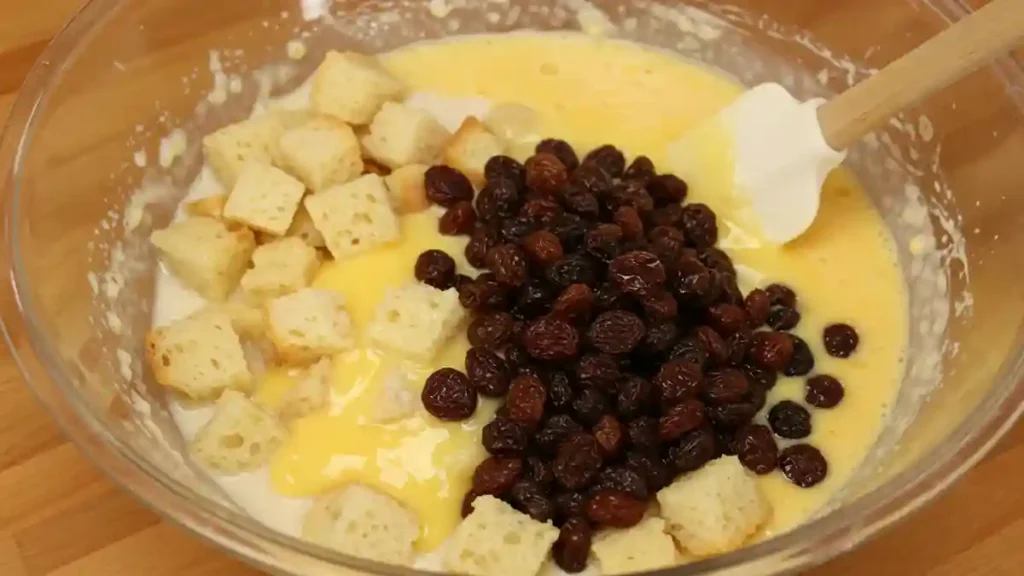 Préparation d’un pudding au pain avec raisins secs, morceaux de pain et crème aux œufs