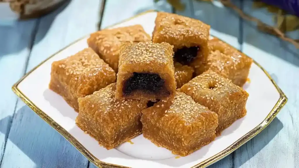 Gros plan sur des makrouts au miel, fourrés aux dattes, parsemés de graines de sésame et joliment dressés sur une assiette blanche.