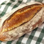 Pain bâtard artisanal à croûte dorée sur un torchon à carreaux