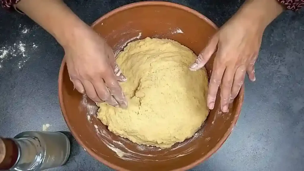 Pétrissage de la pâte à makrout dans un grand plat en terre cuite, réalisé à la main avec de la semoule.