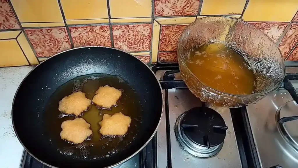 Cuisson des makrouts dans une poêle d’huile chaude, avec un bol de miel fondu à côté sur le feu.