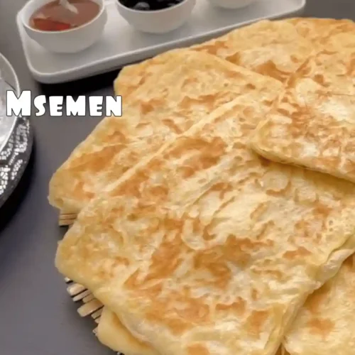 Pile de msemen marocains dorés, servis pour le petit-déjeuner avec thé et olives.