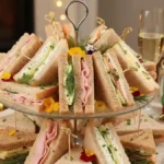 Pain surprise maison garni de mini sandwiches au jambon, fromage frais et concombre, présenté sur un plateau à étages, ambiance festive